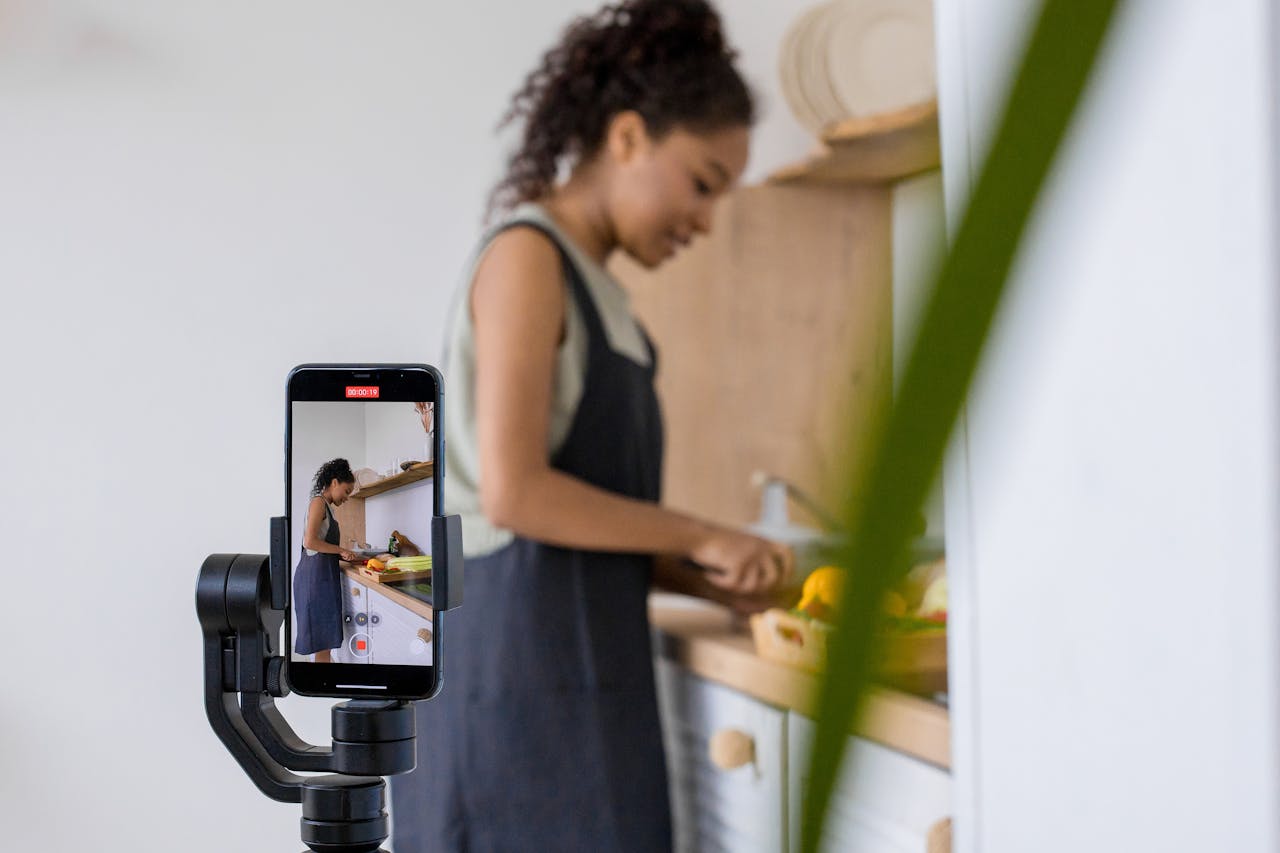 A woman records a cooking tutorial on a smartphone with stabilizer. Modern kitchen setting.